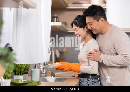Mari coréen aimant soutenant la femme pendant qu'elle lave la vaisselle Banque D'Images