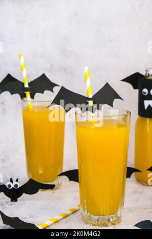 Queues de macktails d'Halloween. Cocktail orange sans alcool pour Halloween sur table blanche. Les pailles sont décorées de battes en papier coupées. Banque D'Images