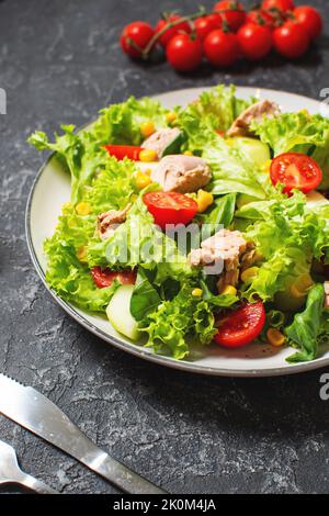 Salade de thon avec laitue, tomates cerises, concombre et maïs sur fond de pierre noire Banque D'Images