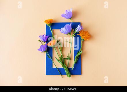 Fleurs bleues et fleurs orange calendula dans un cadre bleu sur fond orange. Posé à plat d'été Banque D'Images