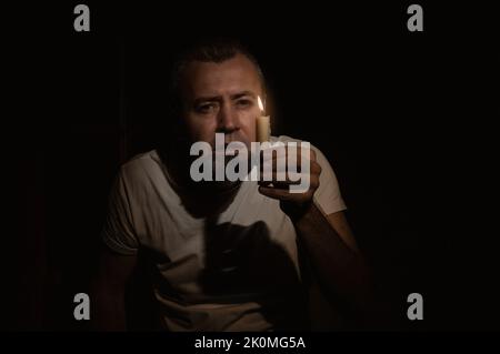 Homme effrayé avec une bougie pendant la coupure. Homme regardant l'appareil photo avec une bougie dans l'obscurité. Concept d'interdiction. Banque D'Images