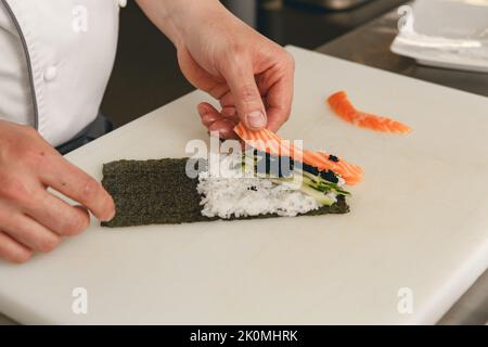 Le chef prépare des sushis au riz, au saumon et au nori dans la cuisine du restaurant japonais Banque D'Images
