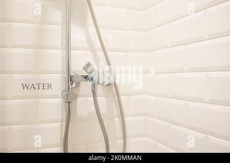 Robinet moderne en acier inoxydable au coin d'une cabine de douche carrelée de blanc Banque D'Images