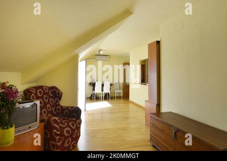 salle de séjour avec canapé deux places avec tissus gris, fenêtres blanches avec rideaux, table à manger avec chaises blanches et meubles en bois, chaise à oreilles et inclinée Banque D'Images