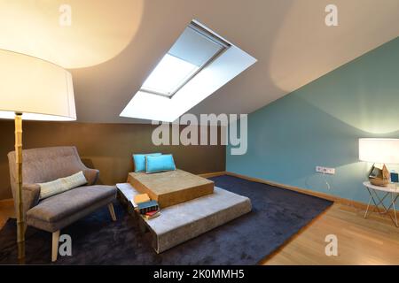 Coin lecture de la chambre avec chaise à dossier sous la lampe, tapis de cerf foncé et divan sous la lucarne au plafond incliné Banque D'Images