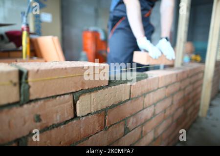 Un constructeur professionnel pose des briques et construit un mur dans l'appartement Banque D'Images