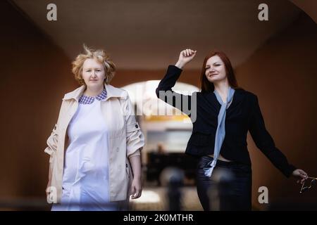 Deux femmes ensemble - blonde dans la lumière et tête rouge dans les vêtements sombres marchent ensemble sur le fond de l'arche. Banque D'Images