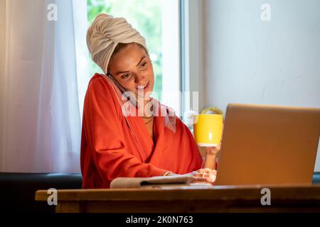 Image symbolique Precrastination, la jeune femme tente de faire beaucoup de choses en même temps, après le bain, sur l'ordinateur, téléphone, journal, et le petit déjeuner Banque D'Images