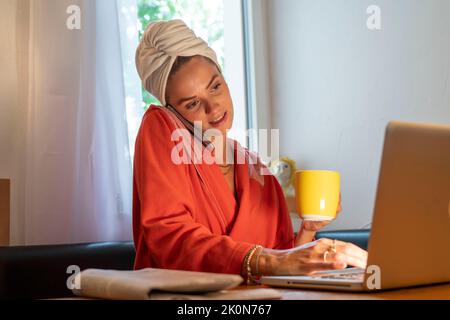 Image symbolique Precrastination, la jeune femme tente de faire beaucoup de choses en même temps, après le bain, sur l'ordinateur, téléphone, journal, et le petit déjeuner Banque D'Images