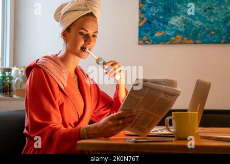 Image symbolique Precrastination, la jeune femme tente de faire beaucoup de choses en même temps, après le bain, sur l'ordinateur, téléphone, journal, et le petit déjeuner Banque D'Images