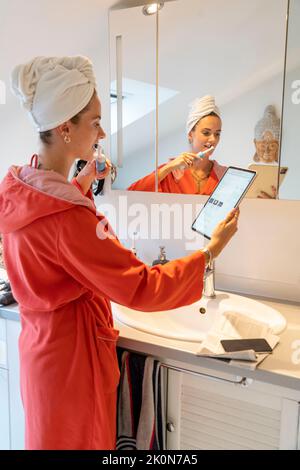 Image symbolique Precrastination, jeune femme essayant de faire beaucoup de choses à la fois, dans la salle de bains, sur l'ordinateur, parler au téléphone, lire les nouvelles Banque D'Images