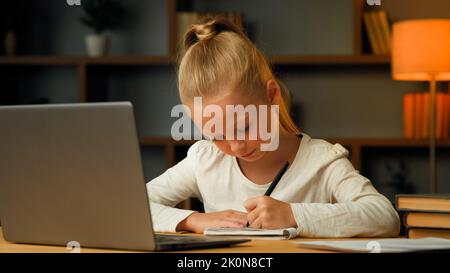 Smart jolie fille primaire blonde petit élève sept ans enfant étudiant dans la chambre maison écriture devoirs faire des tâches élémentaires de mathématiques imagerie Banque D'Images