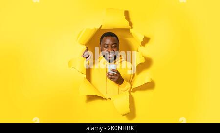 Heureux africain américain homme utilisant le téléphone portable et sourire, debout dans le trou de papier déchiré, panorama Banque D'Images