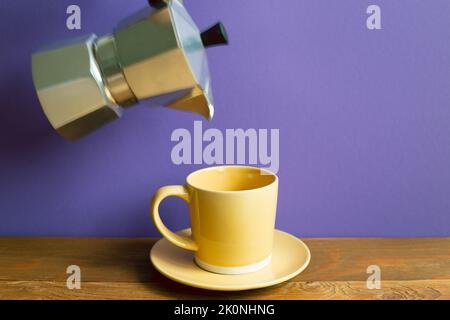 Tasse de café jaune et pot de moka sur table en bois. Fond de mur violet. Style rétro Banque D'Images