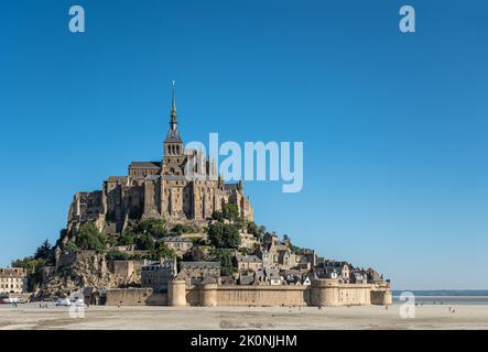 Mont Saint-Michel, Normandie, France - 8 juillet 2022 : la structure en pierre brune de sa roche entourée d'estran sablonneux au ciel bleu. Certains offrent Banque D'Images