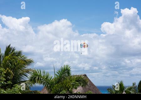 Les touristes en parachute ascensionnel contre le ciel bleu et les nuages blancs survolent les palmiers sur une plage tropicale au Mexique Banque D'Images