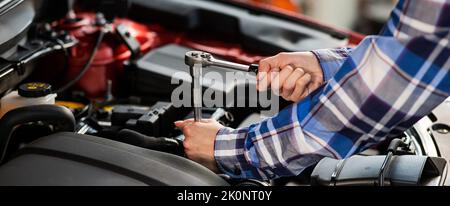 Mécanique automobile femelle en dévissant un écrou pour remplacer une bougie d'allumage de voiture. Banque D'Images