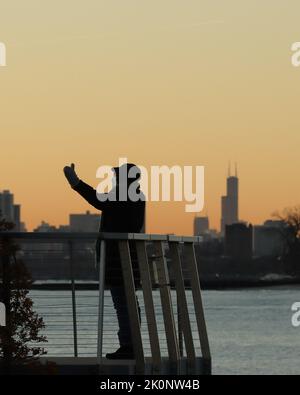 L'homme sur une jetée accueille le soleil du matin avec l'horizon de la ville de Chicago en arrière-plan Banque D'Images