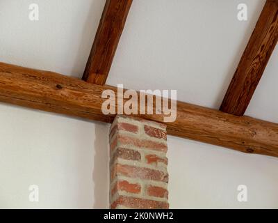 Poteau en pierre de brique rouge comme structure de soutien dans une vieille maison. La traverse en bois du toit est soutenue. Le détail architectural est visible. Banque D'Images