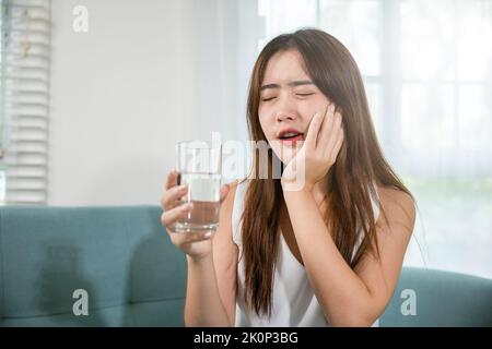 Belle femme mal de dents et problèmes dentaires touchant la joue sensation de douleur après avoir bu de l'eau froide, jeune femme asiatique avec des dents sensibles tenant g Banque D'Images