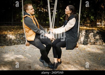 Jeune couple interracial souriant heureux sur swing, femme asiatique, homme caucasien en plein air Banque D'Images