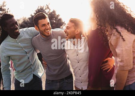 groupe multi-ethnique d'amis positifs qui se embrasent et s'amusent à l'extérieur. Les jeunes souriants qui rient ensemble apprécient la communauté - des millénaires joyeux Banque D'Images
