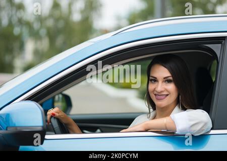 Le chauffeur de femme adulte aux cheveux noirs est assis dans une voiture bleue souriant Banque D'Images