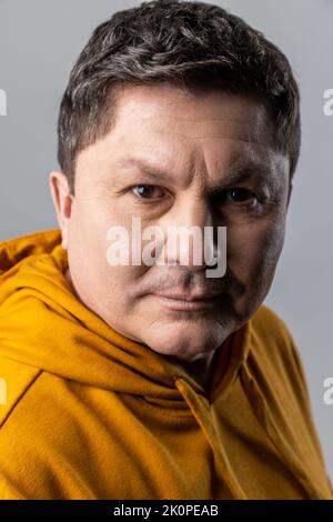 Portrait en gros plan d'un homme élégant et confiant qui regarde l'appareil photo avec une expression calme, des soins de santé et de beauté masculins, portant un sweat à capuche de style urbain. Prise de vue en studio isolée sur fond gris. Banque D'Images