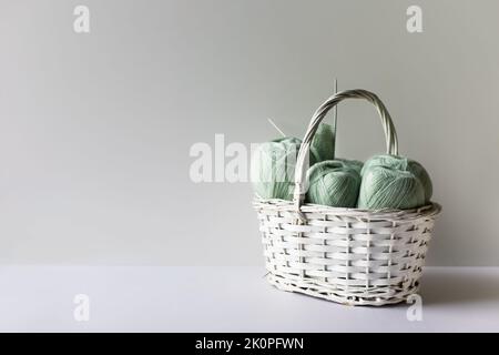 Fils vert clair dans un panier blanc sur fond gris avec aiguilles à tricoter. Banque D'Images