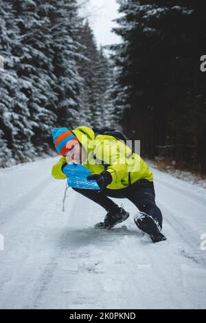 Portrait franc d'un jeune homme portant une veste de randonnée d'hiver jaune, des échauffements et une casquette blanche pendant la saison d'hiver dans une zone enneigée. Pilotage d'une plas Banque D'Images