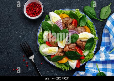 Salade Périgord avec foie de poulet, tomates, concombres, œufs, laitue et épinards. Arrière-plan de la table de cuisine noire, vue du dessus Banque D'Images