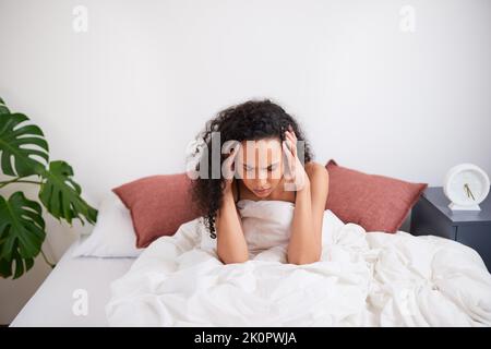 Une jeune femme multi-ethnique s'assoit avec la tête dans les mains luttant pour se réveiller au lit Banque D'Images