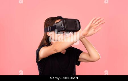Femme portant un casque de réalité virtuelle, fond rose. Banque D'Images