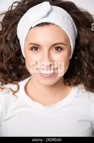 Belle jeune femme aux cheveux bouclés portant un bandeau blanc tout en regardant l'appareil photo et en souriant. Une femme gaie avec une peau parfaite exprimant des émotions positives. Banque D'Images