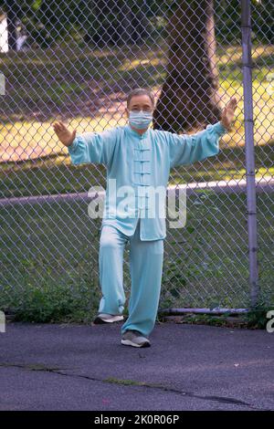 Un homme d'âge moyen portant un masque et un peignoir de Tai Chi mène une classe matinale dans un parc à Queens, New York. Banque D'Images