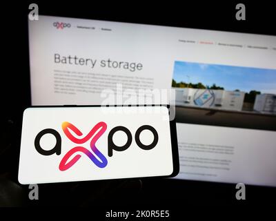 Personne tenant un smartphone avec le logo de la société suisse de l'énergie Axpo Holding AG à l'écran devant le site. Mise au point sur l'affichage du téléphone. Banque D'Images