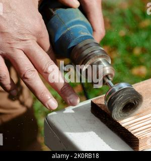 La main mâle tient la machine à brosser tournant électrique avec disque métallique sablant un morceau de bois. Banque D'Images