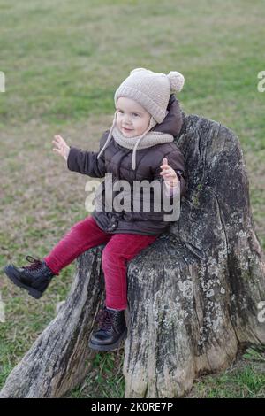 Fille jouant sur un vieux moignon d'arbre dans un parc public Banque D'Images