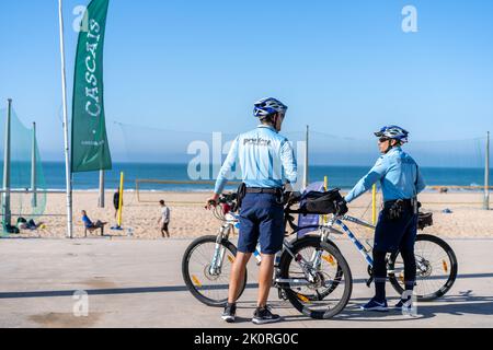 Portugal, Carcavelos avril 2022 deux policiers patrouillent la promenade du bord de mer à vélo. Les gens brûlent le soleil sur la plage publique de la ville, sur l'Atlantique Banque D'Images