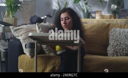 Femme atteinte d'atrophie musculaire de la colonne vertébrale assise sur un canapé à la maison à la table et dessin avec un crayon numérique dans son temps libre Banque D'Images