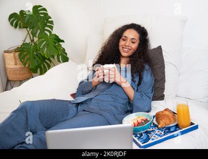 Une jeune femme regarde des films au lit tout en prenant un brunch comme soin de soi Banque D'Images