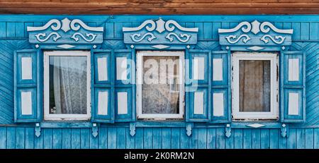 Vieilles fenêtres en bois bleu avec des architraves sculptées et des volets sur la façade en bois de la maison à Buryatia Banque D'Images