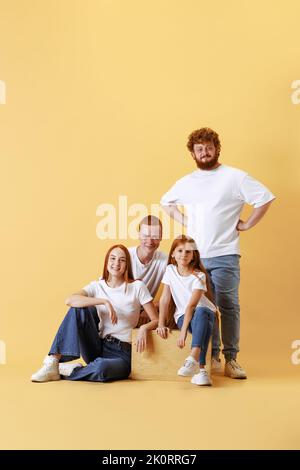 Famille amicale, tête rouge jeunes hommes, femme et enfant portant des vêtements décontractés passer du temps ensemble à la séance photo en studio. Banque D'Images