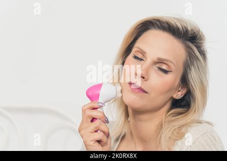 Belle jeune femme caucasienne utilisant un masseur électrique anti-vieillissement pour la peau du visage et un nettoyant pendant sa routine de soin de la peau du matin. Photo de haute qualité Banque D'Images