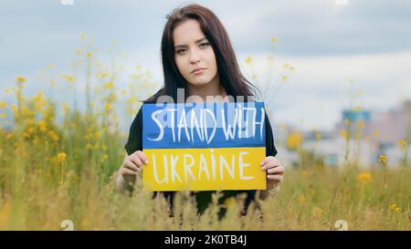 Triste femme ukrainienne fille immigrée femme bouleversée dame posant dans le champ extérieur coloré écrit carton stand avec Ukraine slogan démontre national Banque D'Images