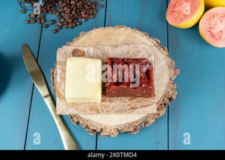 Gros plan de la goyave sucrée avec du fromage sur une planche en bois, à côté d'un couteau, d'une tasse et de grains de café vue de dessus. Banque D'Images