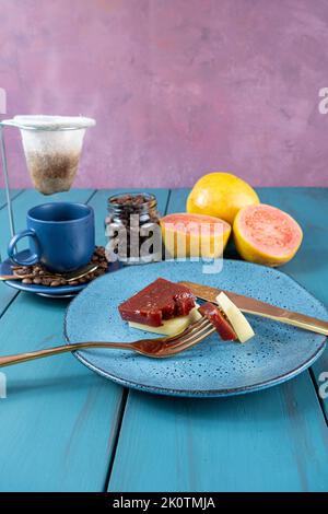 Fourchette avec morceaux de goyave sucrée avec fromage reposant sur l'assiette, à côté des haricots et une tasse de café vue côté. Banque D'Images