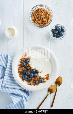 Yaourt. Yaourt grec avec granola et bleuets frais dans un bol blanc sur fond de vieux bois blanc. Concept petit déjeuner. Une alimentation saine pour le petit-déjeuner Banque D'Images