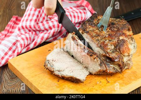 Viande de porc cuite avec épices tranchées sur une planche à découper brune avec couteau et fourchette. Viande grillée. L'homme coupe un morceau de viande sur des tranches avec un couteau. Banque D'Images