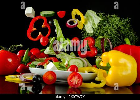 Salade fraîche avec ingrédients volants sur fond noir. Salade flottante, poivrons, tomates, oignons et fromage dans l'air au-dessus de l'assiette. Banque D'Images